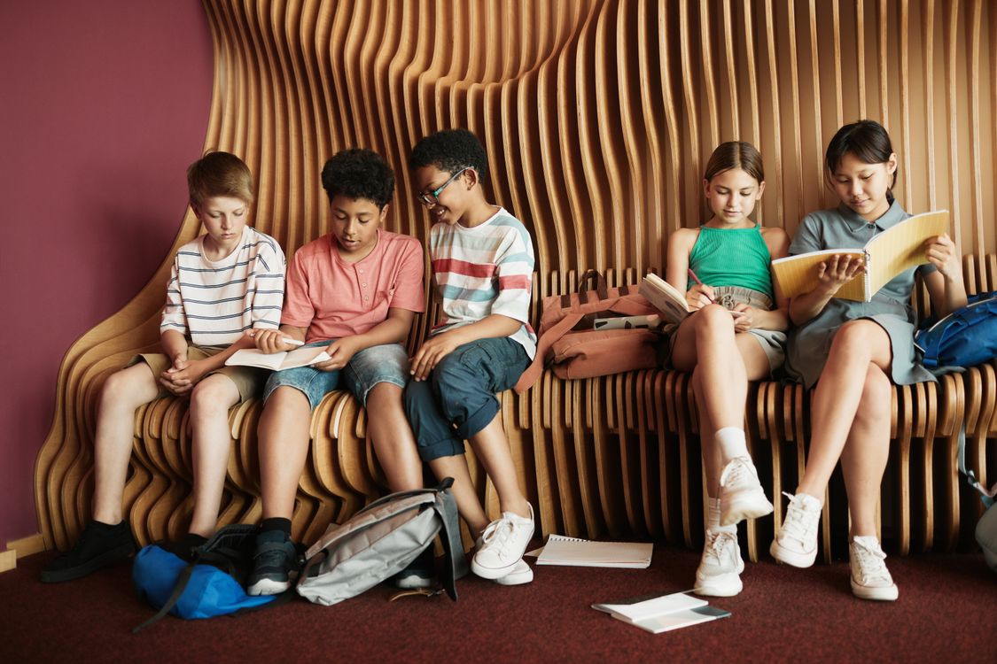 Eine vielfältige Gruppe von Kindern liest gemeinsam ein Buch auf einer Bank