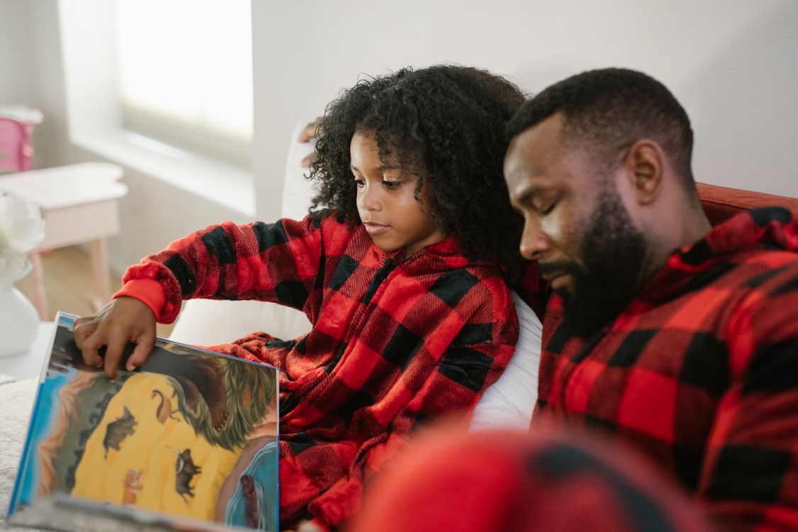 Vater und Tochter lesen gemeinsam ein Buch auf dem Sofa