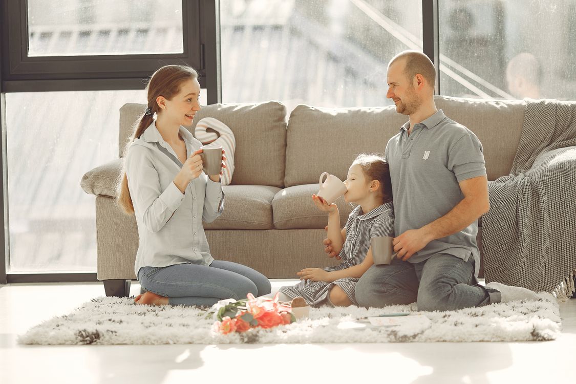 Familie lacht gemeinsam zu Hause auf dem Sofa, der Moment, in dem Urlaubserinnerungen geteilt werden