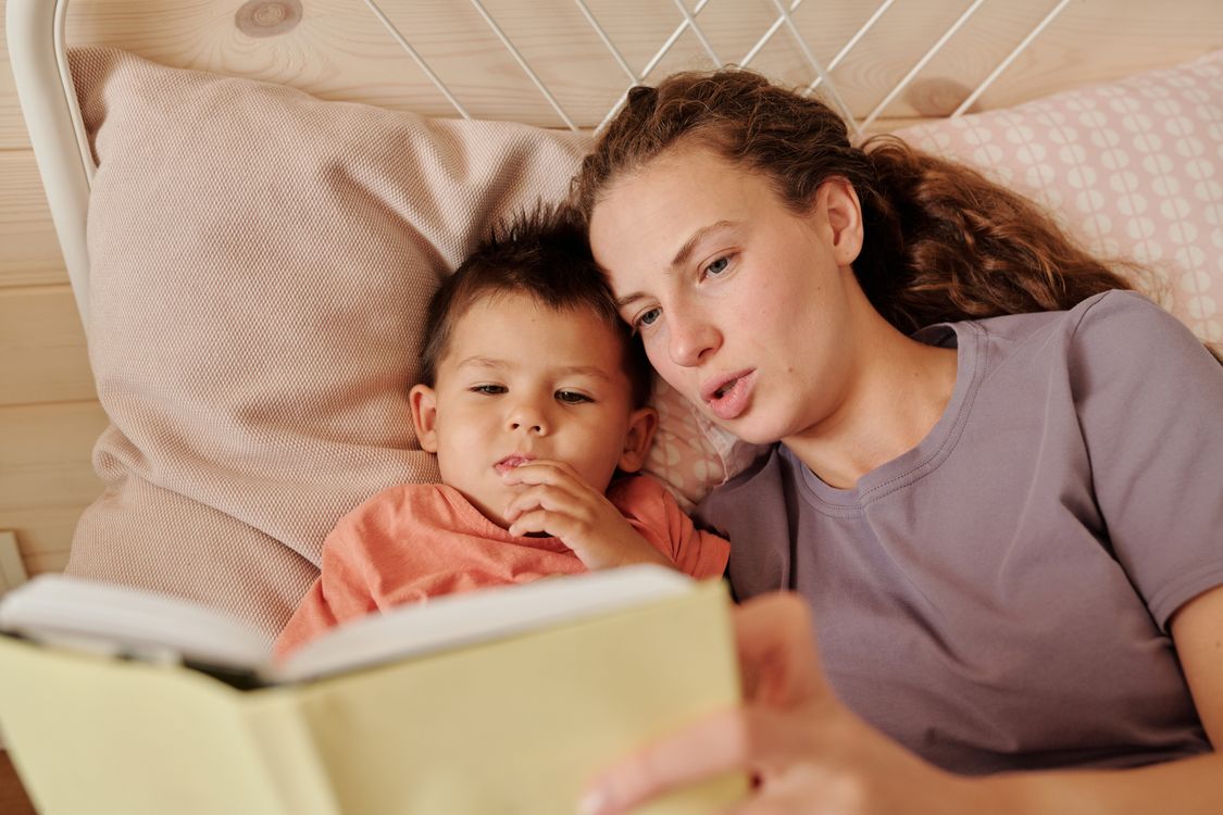 Elternteil liest einem Kind in einem gemütlichen Schlafzimmer eine vertraute Gutenachtgeschichte vor